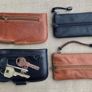May include: Four leather key cases in various colors: brown, black, and tan. Each case has a zippered closure and some include a wrist strap. One black case is open, displaying several keys.