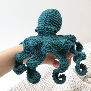 May include: A teal crocheted octopus with black eyes. The octopus has eight tentacles that are curled and twisted.