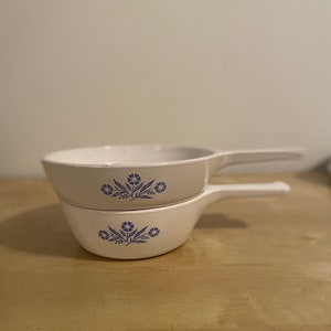 May include: Two white ceramic baking dishes with blue floral designs. The dishes are stacked on top of each other.