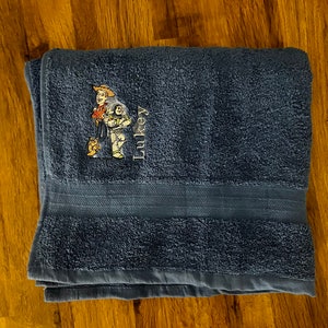 Puede incluir: Una toalla de baño azul con una imagen bordada de Woody y Buzz Lightyear de la franquicia de películas Toy Story. La toalla tiene el nombre "Luke" bordado.