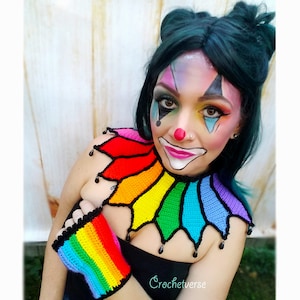 May include: A rainbow crochet collar and matching wrist cuffs with black trim and dangling black beads. The collar is styled as a clown collar with pointed edges. The model is wearing the collar and cuffs and has clown makeup on.