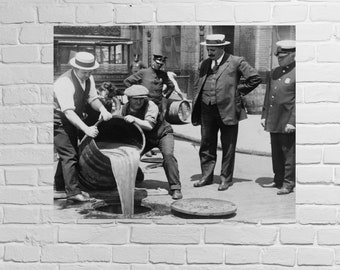 May include: A black and white photo of four men in a street. Two men are pouring liquid from a barrel into a sewer drain. Two men are standing and watching. The men are wearing hats and suits.
