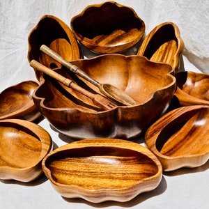 May include: A set of nine wooden bowls in various sizes and shapes, including a large salad bowl with a scalloped edge. The bowls are made of a light brown wood and have a natural, rustic finish.