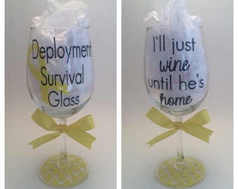 May include: Two clear wine glasses with yellow ribbon bows. The glass on the left has the text "Deployment Survival Glass" on it. The glass on the right has the text "I'll just wine until he's home" on it.