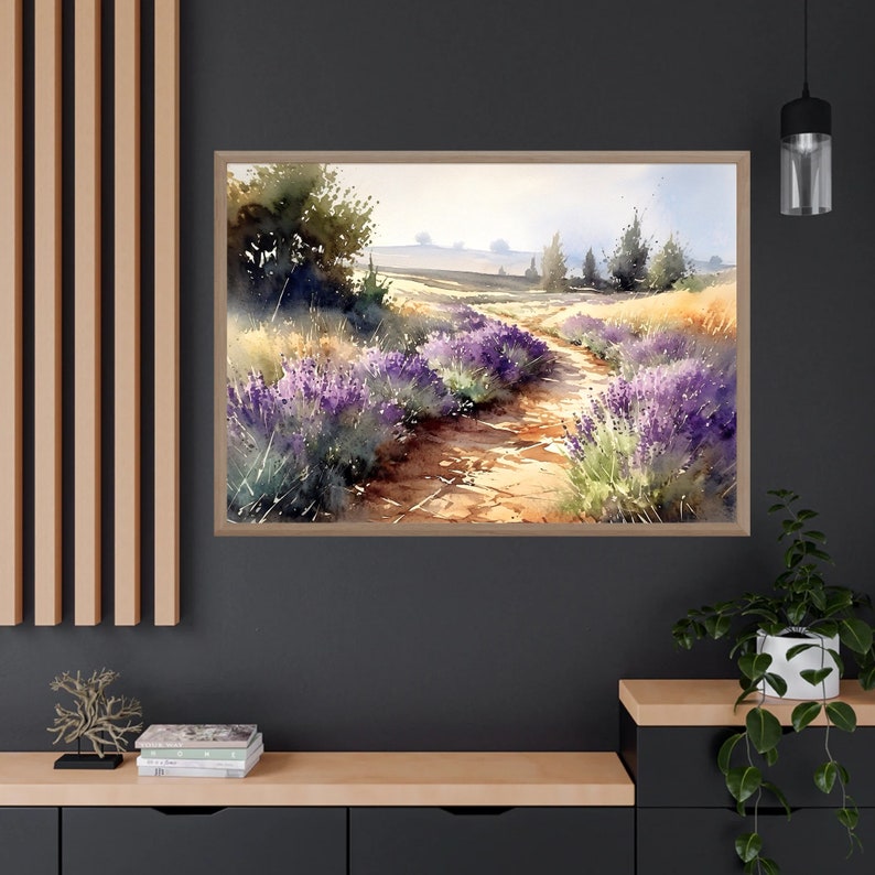May include: A watercolour painting of a path through a field of lavender flowers. The path is dirt and leads to a distant horizon. The sky is a light blue with some clouds. The painting is framed in a light wood frame.