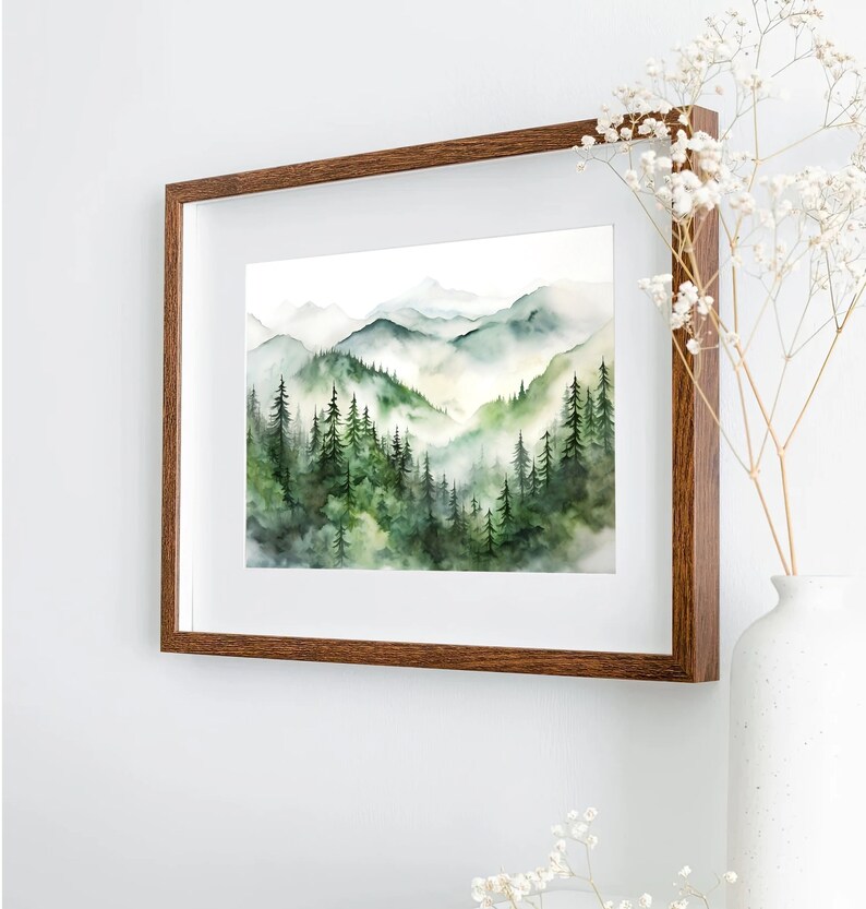 Puede incluir: Pintura a la acuarela de un paisaje monta&ntilde;oso con &aacute;rboles de hoja perenne y valles brumosos. La obra de arte est&aacute; enmarcada en un marco de madera marr&oacute;n oscuro y se exhibe en una pared blanca. La pintura presenta tonos de verde y azul.