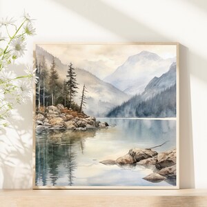 Op de afbeelding: Een aquarel schilderij van een bergmeer sc&egrave;ne met een klein eiland op de voorgrond. Het meer is omringd door bergen en bomen, en het water is lichtblauw. De lucht is lichtgrijs, en er zijn wolken in de lucht.