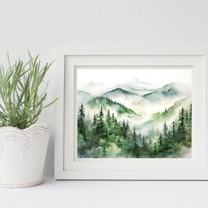 Puede incluir: Una pintura de acuarela enmarcada de un paisaje monta&ntilde;oso. La obra presenta capas de monta&ntilde;as verdes y azules con un bosque de &aacute;rboles de hoja perenne en primer plano. La pintura est&aacute; en un marco blanco.
