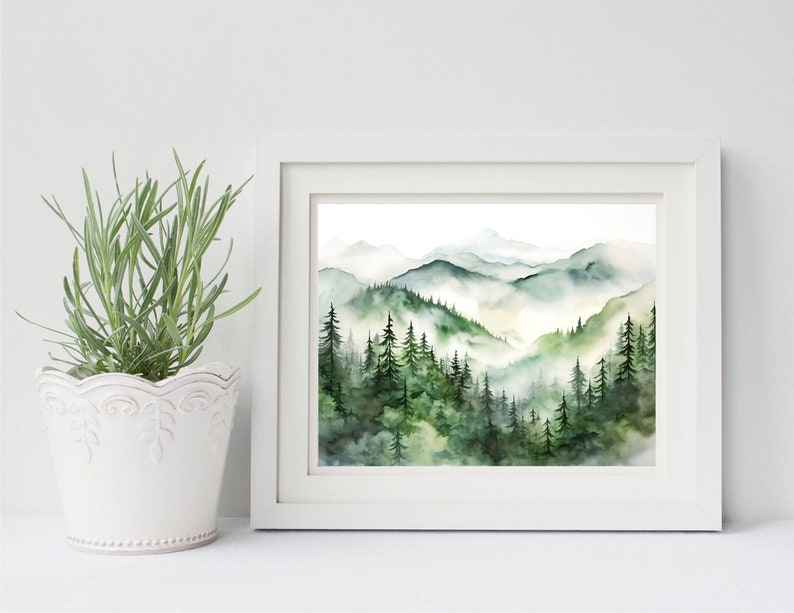 Puede incluir: Una pintura de acuarela enmarcada de un paisaje monta&ntilde;oso. La obra presenta capas de monta&ntilde;as verdes y azules con un bosque de &aacute;rboles de hoja perenne en primer plano. La pintura est&aacute; en un marco blanco.