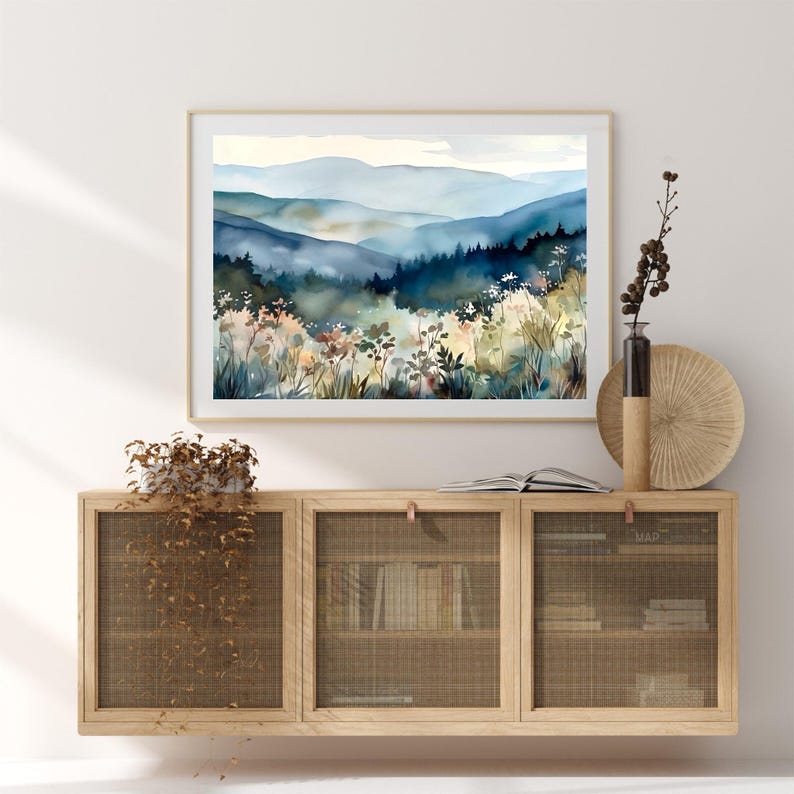 May include: A watercolor painting of a misty mountain landscape with a blue and green color scheme. The painting features a series of rolling hills and a foreground of wildflowers.