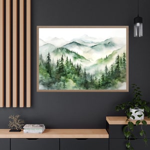 Puede incluir: L&aacute;mina art&iacute;stica de paisaje en acuarela con una escena monta&ntilde;osa brumosa con &aacute;rboles de hoja perenne en tonos verdes y azules. La obra de arte est&aacute; enmarcada en un marco de madera marr&oacute;n claro, ideal para la decoraci&oacute;n del hogar.