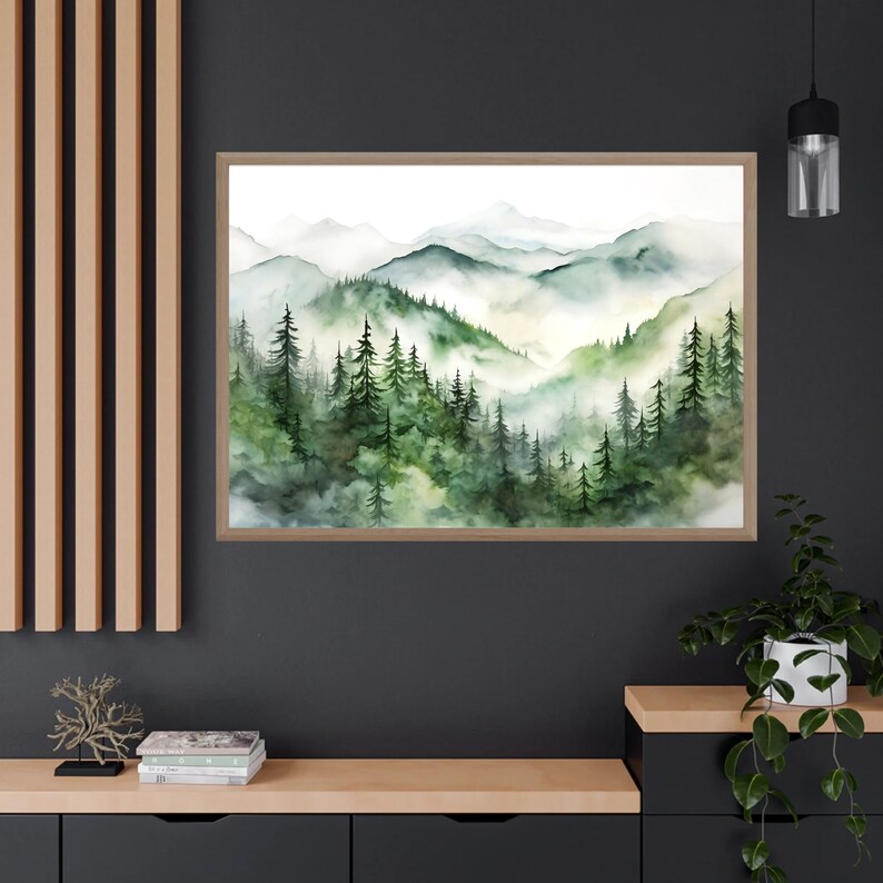 Puede incluir: L&aacute;mina art&iacute;stica de paisaje en acuarela con una escena monta&ntilde;osa brumosa con &aacute;rboles de hoja perenne en tonos verdes y azules. La obra de arte est&aacute; enmarcada en un marco de madera marr&oacute;n claro, ideal para la decoraci&oacute;n del hogar.