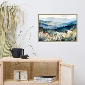 May include: A watercolor painting of a misty mountain landscape with a foreground of wildflowers and greenery. The painting is framed in a light brown frame.