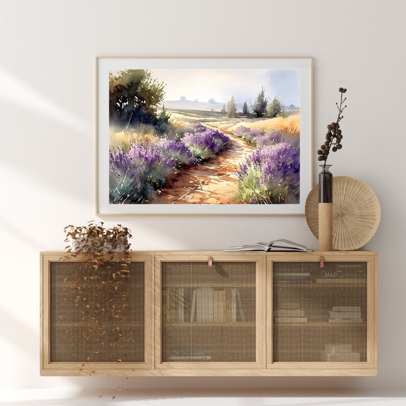May include: A watercolour painting of a lavender field with a dirt path leading through it. The painting is framed and hanging on a white wall above a wooden cabinet with a wire mesh front.