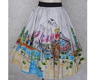 May include: A white full circle skirt with a colorful hand-painted scene of a mountain, a donkey pulling a cart, and two figures. The skirt has a black waistband.