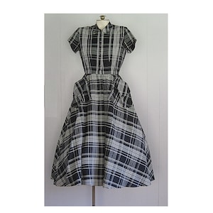 May include: A black and white plaid dress with a button-up front and short sleeves. The dress has a full skirt and pockets on the sides.