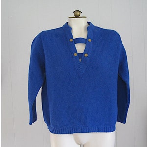 May include: A royal blue knitted sweater with a deep V-neck and a decorative lacing detail with gold buttons.