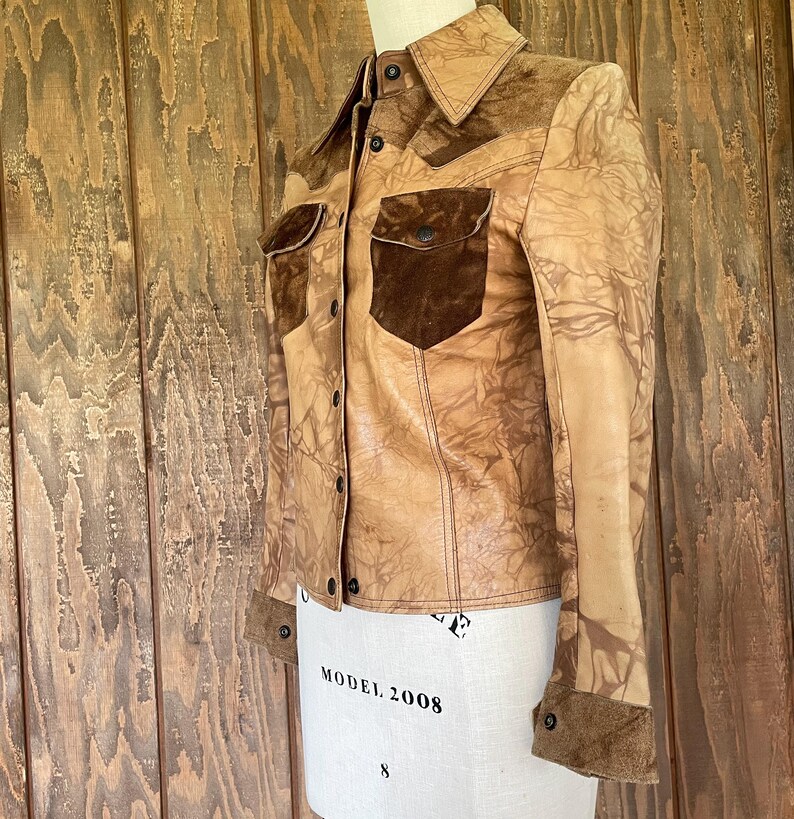 Peut inclure: Une veste en cuir marron avec un col et des poches en daim. La veste a un aspect vieilli avec un motif marbr&eacute;.