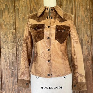 Peut inclure: Une veste en cuir marron avec des accents en daim et un devant boutonn&eacute;. La veste a un motif d&eacute;lav&eacute;, tie-dye.