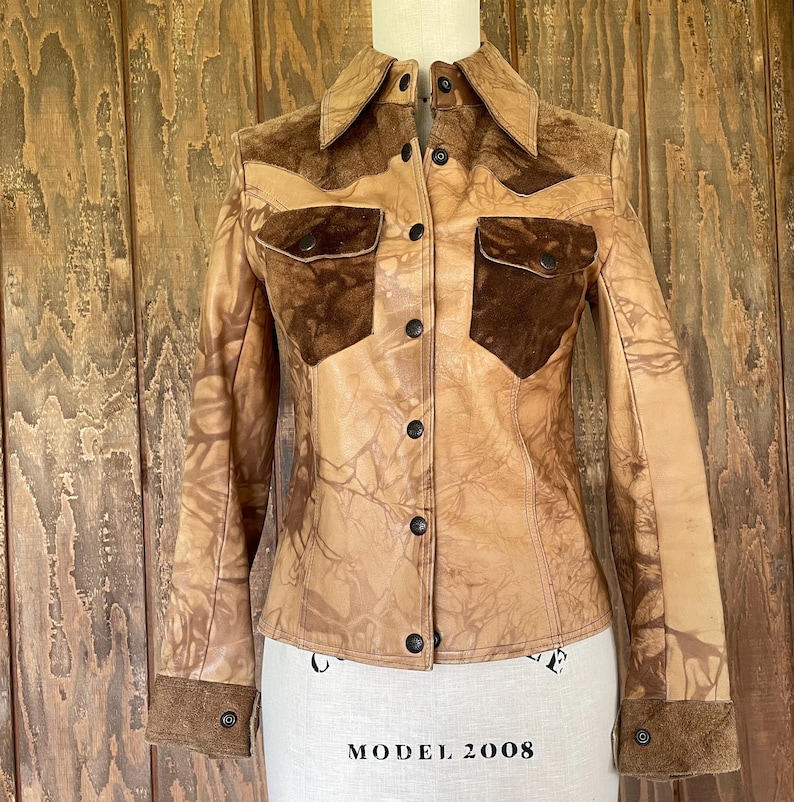 Peut inclure: Une veste en cuir marron avec des accents en daim et un devant boutonn&eacute;. La veste a un motif d&eacute;lav&eacute;, tie-dye.