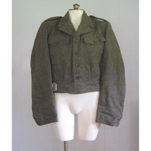 May include: A green wool military jacket with a button-up front and a belt. The jacket has two large pockets on the front and a small pocket on the left sleeve.