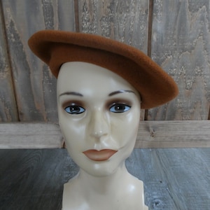 May include: A brown felt beret hat on a mannequin head.