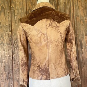 Peut inclure: Une veste en cuir marron avec un empi&egrave;cement en daim et un motif tie-dye. La veste a une fermeture boutonn&eacute;e &agrave; l'avant et des manches longues.
