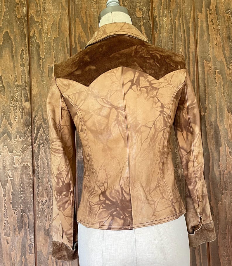 Peut inclure: Une veste en cuir marron avec un empi&egrave;cement en daim et un motif tie-dye. La veste a une fermeture boutonn&eacute;e &agrave; l'avant et des manches longues.