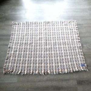 May include: A brown and white houndstooth patterned throw blanket with a fringed edge.