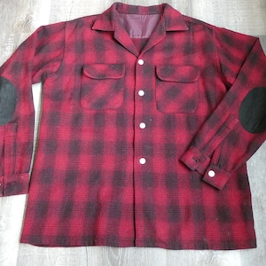 May include: A red and black plaid flannel shirt with elbow patches. The shirt has a button-up front and two chest pockets.