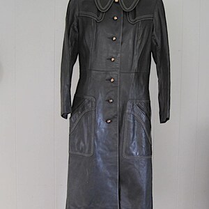 May include: A long black leather coat with a large collar and button closure. The coat has white stitching details and pockets.