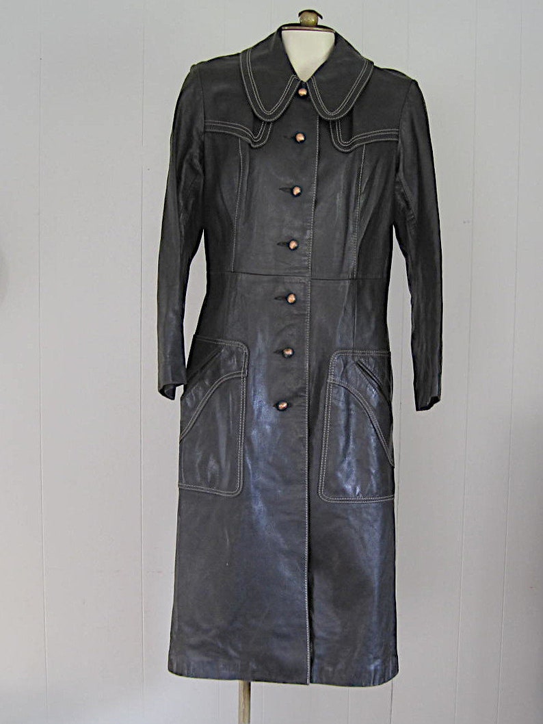 May include: A long black leather coat with a large collar and button closure. The coat has white stitching details and pockets.
