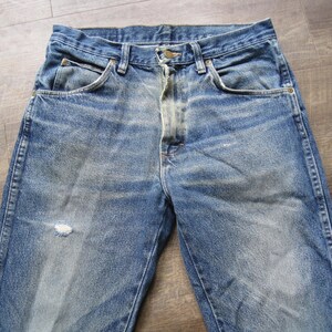 May include: A pair of blue denim jeans with faded areas and a small hole on the left leg.