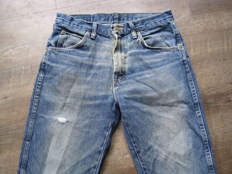 May include: A pair of blue denim jeans with faded areas and a small hole on the left leg.