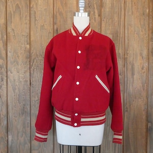 May include: A red varsity jacket with white and tan accents. The jacket has a button-up front, a chest pocket, and white-lined pockets. The collar, cuffs, and waistband feature tan and white stripes. The jacket is displayed on a mannequin.