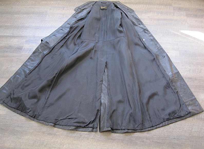 May include: A black leather trench coat with a center back vent and a button closure. The coat is fully lined and has a smooth, silky feel.