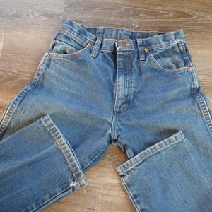 May include: Blue denim jeans with a classic five-pocket design. The jeans have a button and zipper closure, with copper-colored rivets and a straight leg. The denim has a faded appearance, suggesting wear and washing.