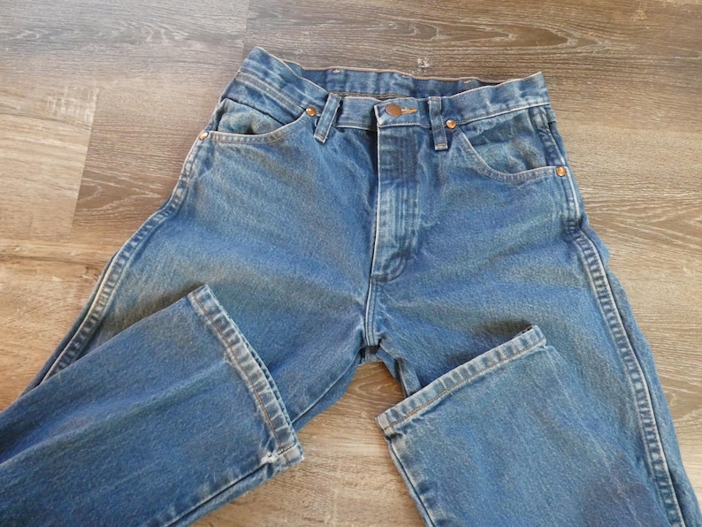 May include: Blue denim jeans with a classic five-pocket design. The jeans have a button and zipper closure, with copper-colored rivets and a straight leg. The denim has a faded appearance, suggesting wear and washing.