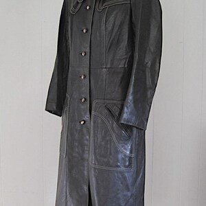May include: A long black leather coat with a large collar and decorative stitching. The coat has a button closure and multiple pockets.