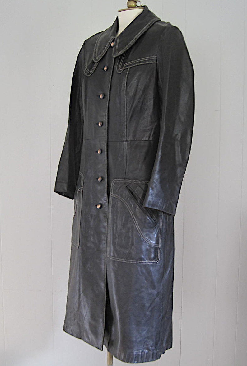 May include: A long black leather coat with a large collar and decorative stitching. The coat has a button closure and multiple pockets.