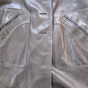 May include: A gray leather jacket with two large pockets on the front. The pockets have white stitching around the edges and a smaller pocket inside each larger pocket.