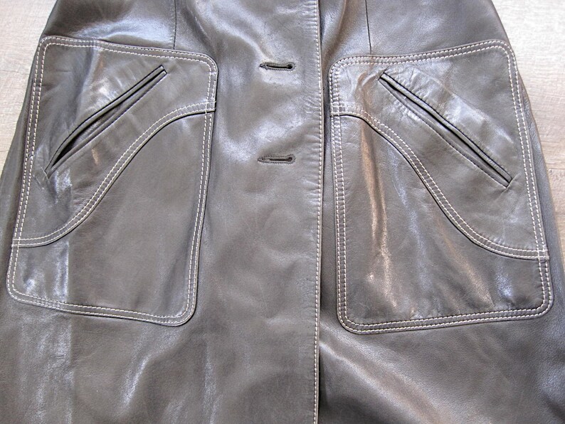 May include: A gray leather jacket with two large pockets on the front. The pockets have white stitching around the edges and a smaller pocket inside each larger pocket.