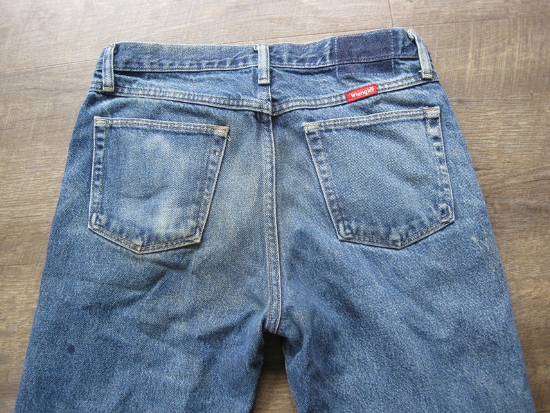 May include: A pair of blue denim jeans with a red Wrangler label on the back pocket.