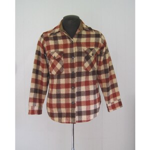 May include: A red, brown, and beige plaid flannel shirt with a collared neckline and long sleeves. The shirt has two chest pockets and a button-up front.