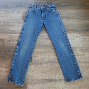 May include: Blue denim jeans with a classic five-pocket design. The jeans have a button and zipper closure, belt loops, and a straight leg fit. The denim has a faded appearance, with lighter areas on the thighs and knees.