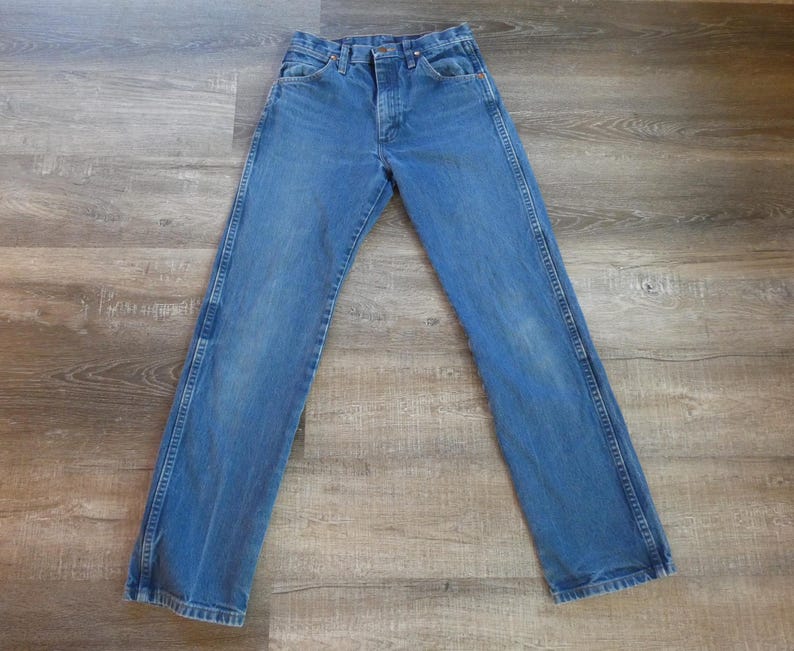 May include: Blue denim jeans with a classic five-pocket design. The jeans have a button and zipper closure, belt loops, and a straight leg fit. The denim has a faded appearance, with lighter areas on the thighs and knees.