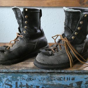 May include: A pair of black leather work boots featuring a high-top design, reinforced toe caps, and metal eyelets for lacing. The boots are equipped with sturdy, multi-colored striped laces and have a worn, textured appearance on the leather surface.