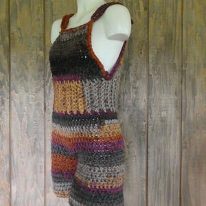 May include: A handmade crochet romper in a variety of colors, including gray, black, orange, and purple. The romper features a striped pattern and a halter-style top with straps. The garment is displayed on a mannequin against a wooden background.