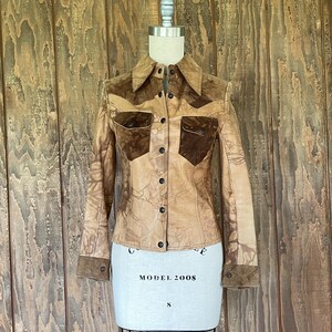 Peut inclure: Une veste en cuir marron avec des accents en daim. La veste a une fermeture boutonn&eacute;e &agrave; l'avant et des manches longues. La veste est sur un mannequin blanc.