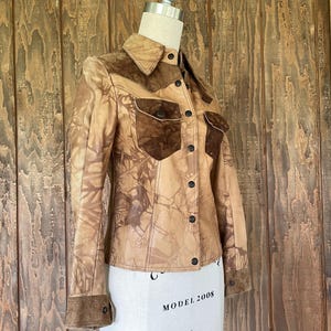 Peut inclure: Une veste en cuir marron avec un col et des poches en daim. La veste a un motif tie-dye et une fermeture boutonn&eacute;e.